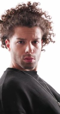 Kıvırcık saçlı küstah bir adam. Arkasına yaslanmış. Gri arka planda ısrarla ileriye bakıyor.