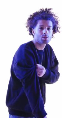 Havalı, kıvırcık saçlı, el ele tutuşan, kol ayarlayan, ileriye bakan ve gri arka planda kendine güvenen moda adamı.