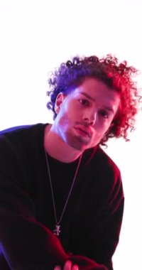 Küstah, kıvırcık saçlı, polis ışıkları önünde rol yapan, kibirli, hareketli, ileriye bakan ve gri arka planda yürüyüp giden genç adamın dikey videosu.