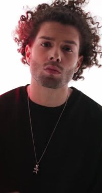 Kıvırcık saçlı, ileriye bakan, dudaklarına ve ağzına dokunan ve gri arka planda yürüyüp giden seksi bir adamın videosunu kapat.