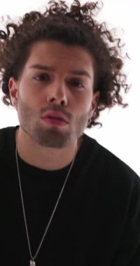 Kıvırcık saçlı ciddi bir adam. Askerî selamlama ve yürüyüp gidiyor. Gri arka planda polis ışıkları açık.