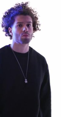 Kendine güvenen, kıvırcık saçlı, parmaklarını öne doğru gösteren, kollarını kavuşturan, ileriye bakan ve gri arka planda dinamik olan yakışıklı bir adam.