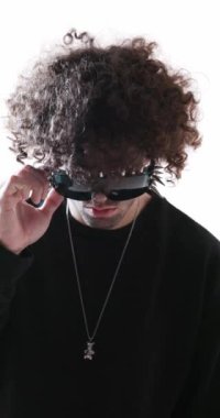 Siyah kapüşonlu havalı genç adam çivili güneş gözlüklerine bakıyor ve flaşlı ışıklarla arka planda avuçlarını ovuyor.