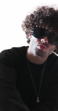 Dikey videoda, siyah kazaklı, sivri güneş gözlüklü havalı bir adamın gri arka planda dans edip eğlendiğini görüyoruz.