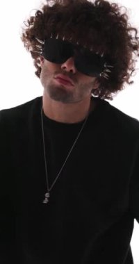 Siyah kazaklı havalı manken öne bakan güneş gözlüklü, gri arka planda dans edip eğleniyor.