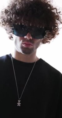 Dikenli güneş gözlüklü, siyah sweatshirt giyen ve gri arka planda ileriye bakan seksi genç adam.