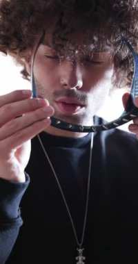 Çekici genç adam çivili gözlükleri indiriyor, ileri bakıyor ve gri arka planda göz kırpıyor.