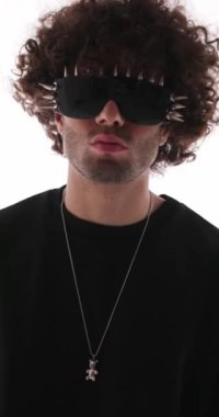 Siyah kapüşonlu, çivili güneş gözlüklü, sessiz jest yapan ve gri arkaplanı dört gözle bekleyen seksi havalı adamın videosunu çek.