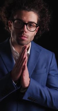 Mavi takım elbiseli seksi iş adamının avuçlarını ovalarken mutlu ve gülümserken siyah arka planda poz verdiği dikey bir video.