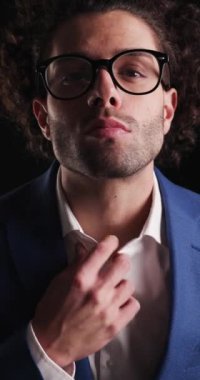 Kıvırcık saçlı seksi iş adamı, gömleğini düzeltiyor, el ele tutuşuyor ve siyah arka planı açarken kendinden emin oluyor.