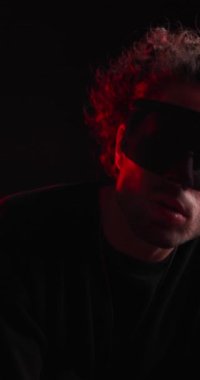 Siyah kapüşonlu dinamik genç adam kollarını kavuşturup dans ediyor, el ele tutuşuyor ve siyah arkaplanı dört gözle bekliyor.