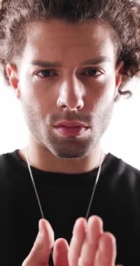 Yakışıklı, kıvırcık saçlı, avuçlarını ovuşturan, ileriye bakan ve stüdyoda gri arka planda havalı olan adam.