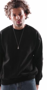 Siyah kapüşonlu kıvırcık saçlı, gri arka planda kollarını açarak bekleyen kendinden emin, rahat bir adamın dikey videosu.