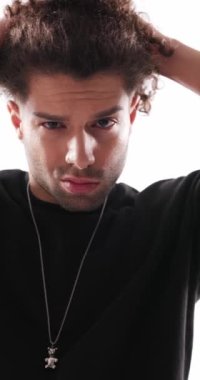 Yakışıklı, sıradan bir adam ileriye bakıyor, el ele tutuşuyor ve gri arka planda kıvırcık saçlarını düzeltiyor.