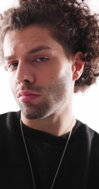 Siyah kapüşonlu, kıvırcık saçlı, ısrarla ileriye bakan ve gri arka planda aptal bir surat yapan çekici genç adamın videosunu kapat.