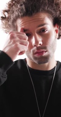 Seksi, kıvırcık saçlı, kaşlarına dokunan, burnuna piercing takan, ağzı olan, sırıtan ve gri arka planda sevimli olan genç adam.