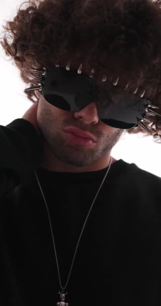 首に手を握るスパイクサングラスを持つセクシーなカジュアルな男の垂直ビデオ 横を見て灰色の背景に傲慢である — ストック動画