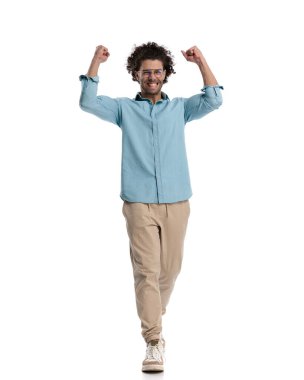 Heyecanlı sıradan adam beyaz arka planda yürürken elleri havada kutlama yapıyor.