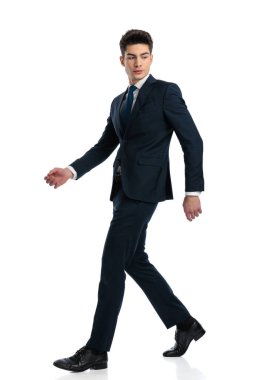 Lacivert takım elbiseli şık bir modacının beyaz arka planda yürüdüğünü ve arkasına baktığını görüyorum.