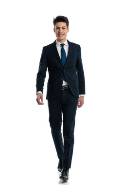Lacivert takım elbiseli yakışıklı bir gencin portresi. Beyaz arka planda gülümsüyor ve yürüyor.