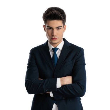 Lacivert takım elbiseli genç bir iş adamı kollarını kavuşturup beyaz arka planda ileriye bakıyor. 