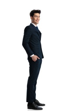 Mutlu genç işadamı sırada bekliyor ve elleri ceplerinde beyaz arka planda gülümsüyor. 