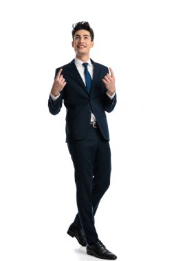 Takım elbiseli mutlu genç adamın tüm vücudu gökyüzünü işaret ediyor, minnettar oluyor ve beyaz arka planda yürüyor. 