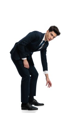 Takım elbiseli zarif genç iş adamı beyaz arka planda yerden bir şey almaya çalışıyor.