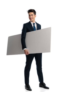 Kolunun altında boş bir tabelayla heyecanlı bir iş adamı beyaz arka planda dikilirken yan yana bakıp gülüyor.