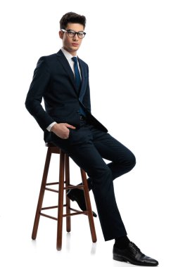 Gözlüklü yakışıklı bir gencin tüm vücudu beyaz arka planda, ahşap koltukta el ele otururken. 