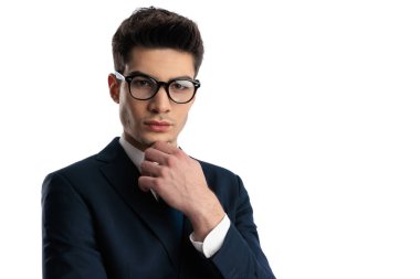 Zarif takım elbiseli düşünceli genç bir adamın portresi. Çeneye dokunuyor ve beyaz arkaplan önünde düşünüyor.