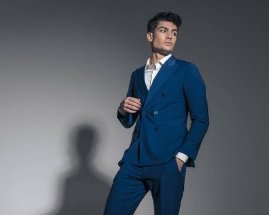 Yakışıklı genç işadamı açık gri arka planda cebini tutarken yan tarafa bakıyor