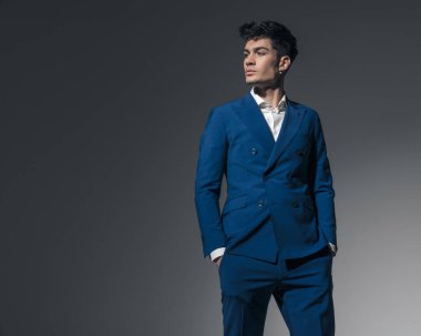 Stüdyonun arka planında elleri ceplerinde duran rahat genç işadamı yan tarafa bakıyor.