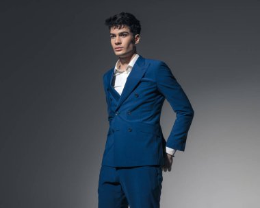 Açık gri arka planda, çift göğüslü mavi takım elbiseli, genç ve seksi adamın el ele tutuşması.