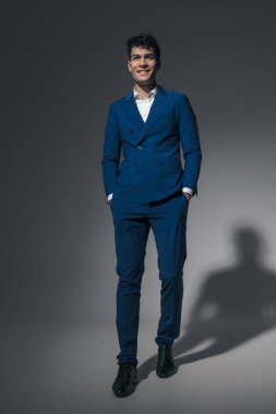 Yakışıklı adam model açık gri arka planda yürürken cepleri tutuyor ve gülümsüyor.