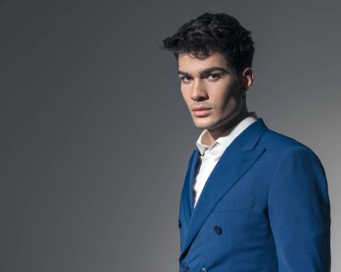 Genç ve yakışıklı adamın portresi. Mavi takım elbise ve gri arka planda beyaz gömlek giyiyor.