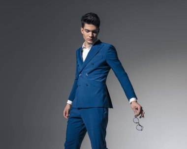 Gri arka planda yana adım atarken gözlüklere yan yana bakan erkek modelinin yakın plan görüntüsü