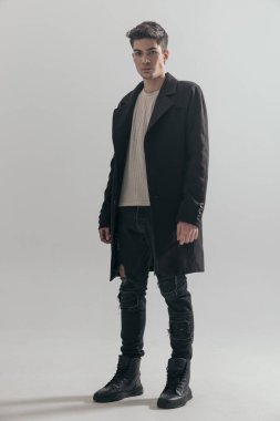 Siyah paltolu genç seksi adam açık gri arka planda duruyor.