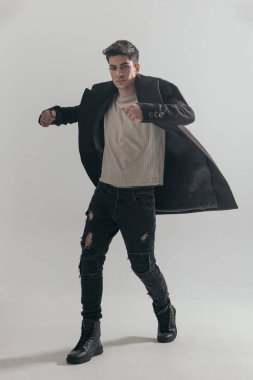 Yakışıklı adam gri arka planda siyah palto giyerken ileri gidiyor.