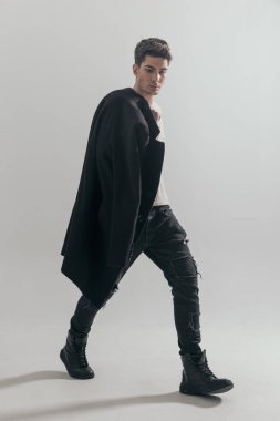 Gri arka planda omuzlarında paltoyla yana doğru yürüyen seksi genç adam.