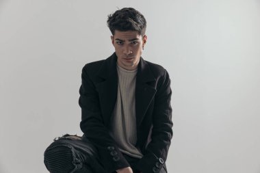 Siyah paltolu, gri arka planda dizleri bükülmüş seksi genç adama yaklaş.