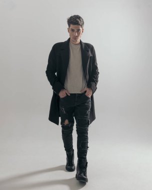 Siyah paltolu seksi bir adam beyaz arka planda yürürken cepleri tutuyordu.