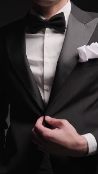 タキシードボタンを保持している若い男性モデルのクローズアップ ポケットに手で黒い背景に立っている間 — ストック動画