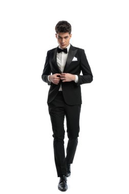 Kibirli, zarif iş adamı, siyah smokinini ilikliyor ve stüdyoda beyaz arkaplan önünde kendinden emin bir şekilde yürüyor.