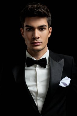 Siyah arka planda duran smokin ve papyon giyen yakışıklı genç adamın portresi.