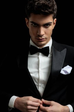 Siyah smokinli ve papyonlu yakışıklı adamın siyah arka planda takım elbisesini düzenlediği yakın plan.