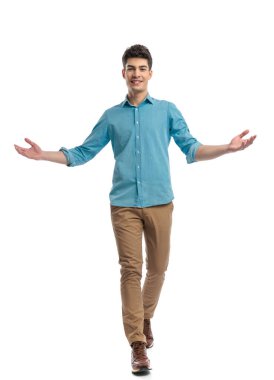 Mavi gömlekli yakışıklı adam beyaz arka planda ilerlerken hoş geldin jesti yapıyor.