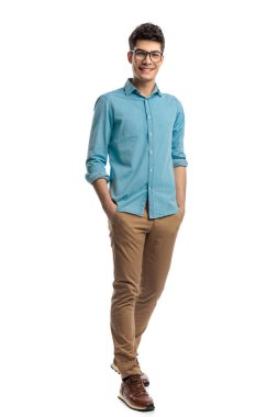 Elleri ceplerinde rahat bir adam beyaz arka planda mavi gömlek ve gözlük takarken öne çıkıyor.