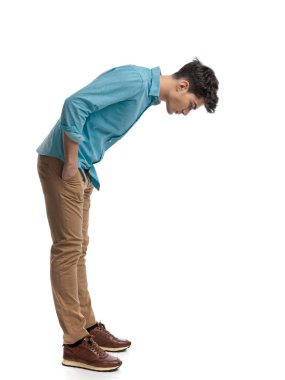 Beyaz arka planda elleri ceplerinde dururken öne eğilip aşağı bakan rahat bir adamın yan görüntüsü.