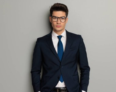 Siyah takım elbiseli rahat iş adamının yakın plan fotoğrafı. Gri arka planda elleri ceplerinde duruyor.